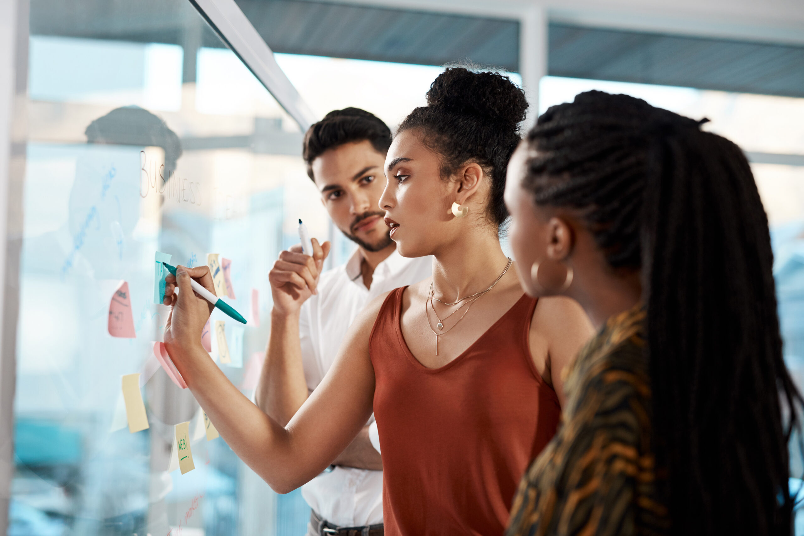 Team members collaborate on a business strategy session, using sticky notes and a glass board to brainstorm ideas, analyze information, and improve decision-making in the workplace.